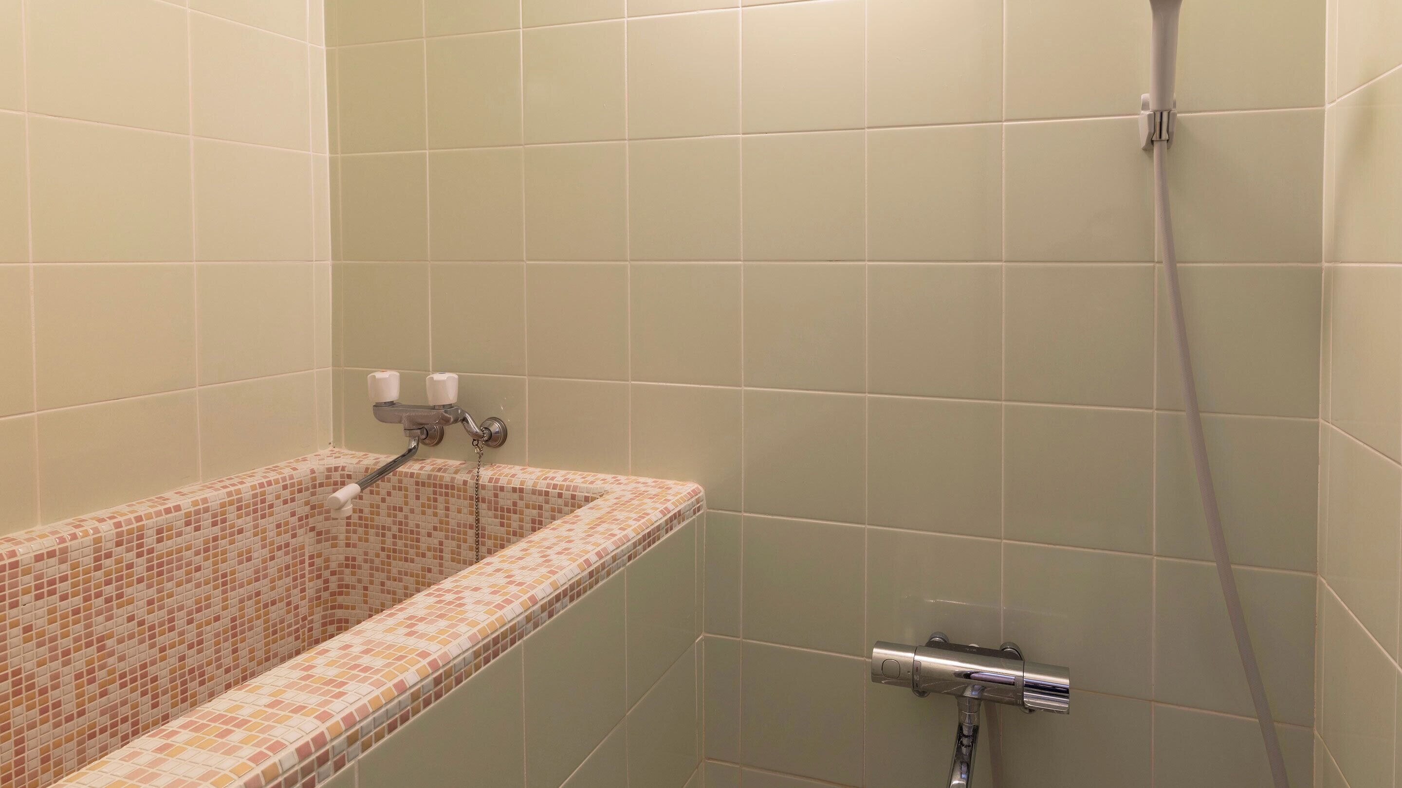 A bathroom with a tiled shower, a bathtub with a mosaic tile design, and a faucet.