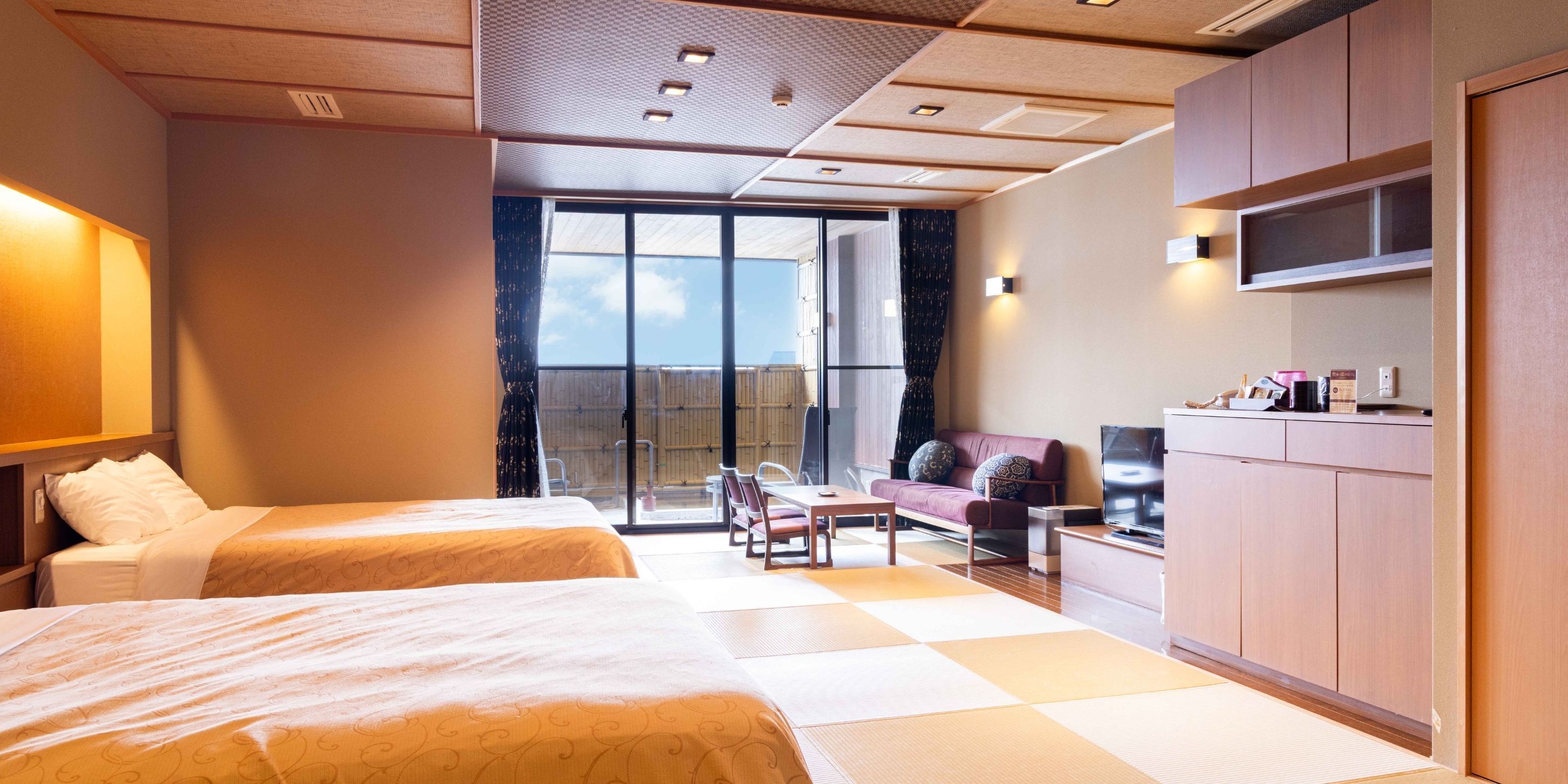 A hotel room with two beds, a sofa, a TV, a desk, and a sliding glass door to the outside.