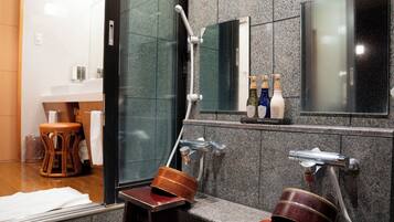 Un baño con cabina de ducha de vidrio, un taburete de madera, una mesita de madera y un espejo sobre el lavabo.