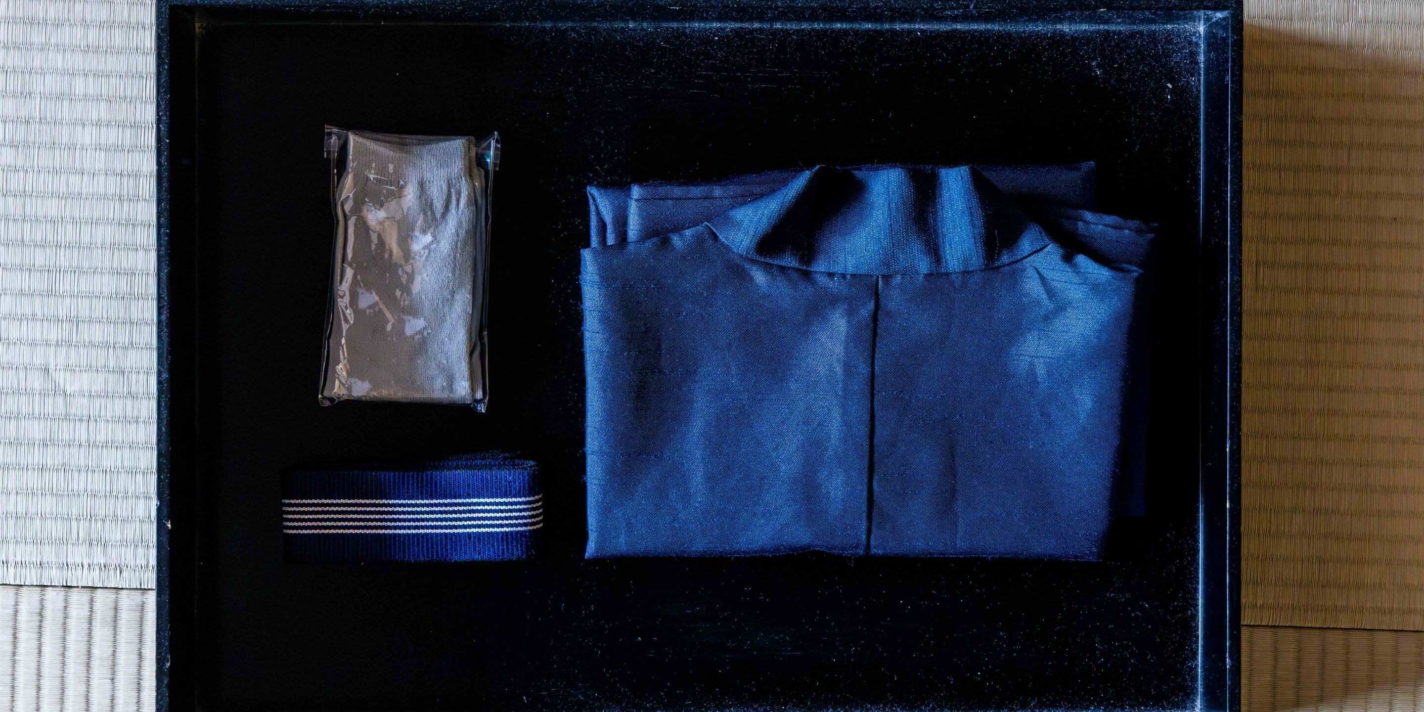 A black box containing a blue shirt, a striped tie, and a small packet.