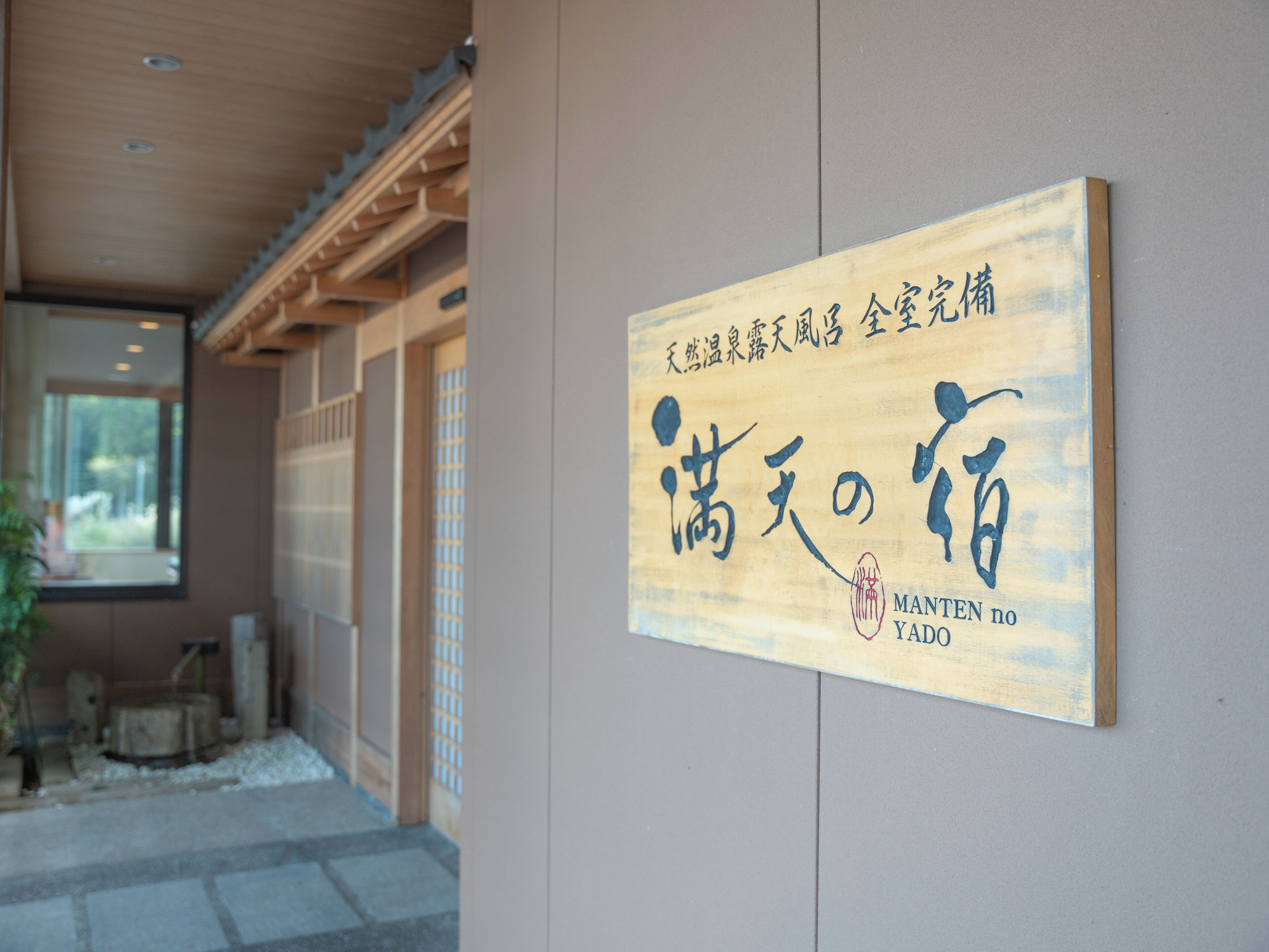 A wooden sign with Japanese characters and the name "Manten no Yado" on a wall.
