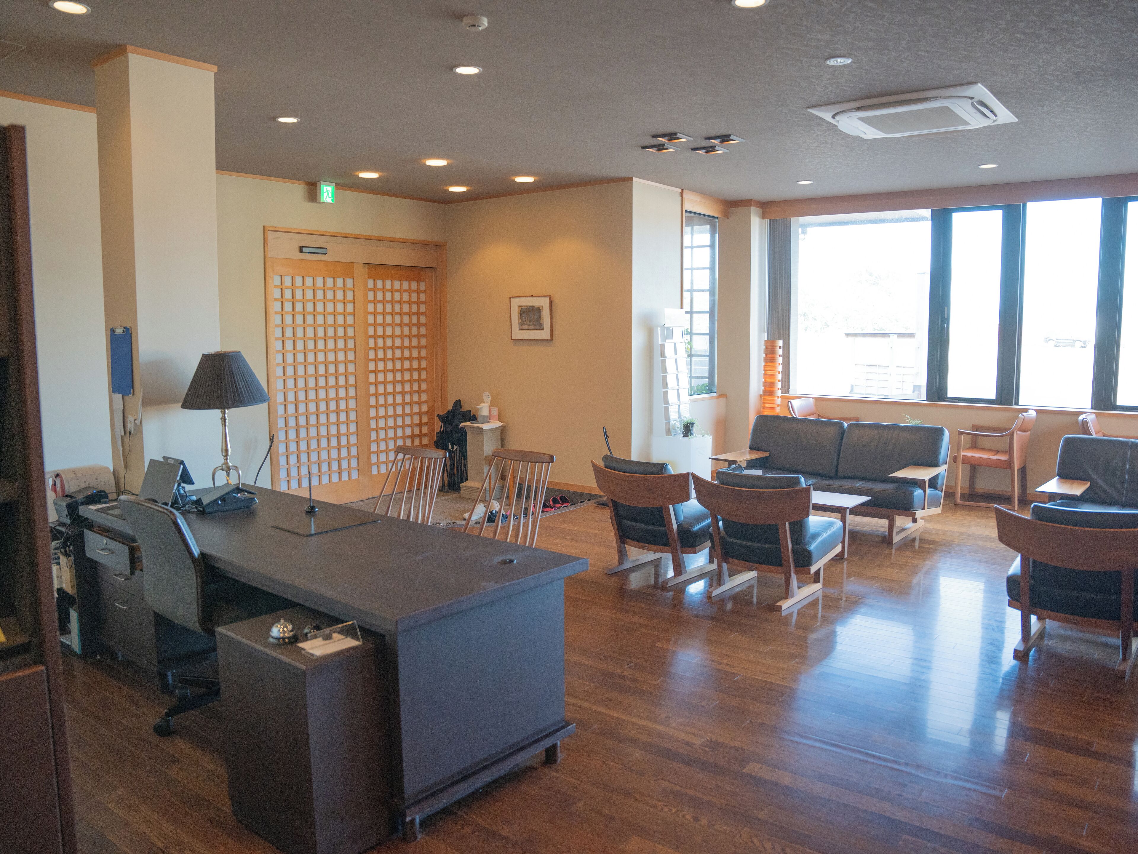 A spacious room with a desk, chairs, a sofa, and a large window providing natural light.