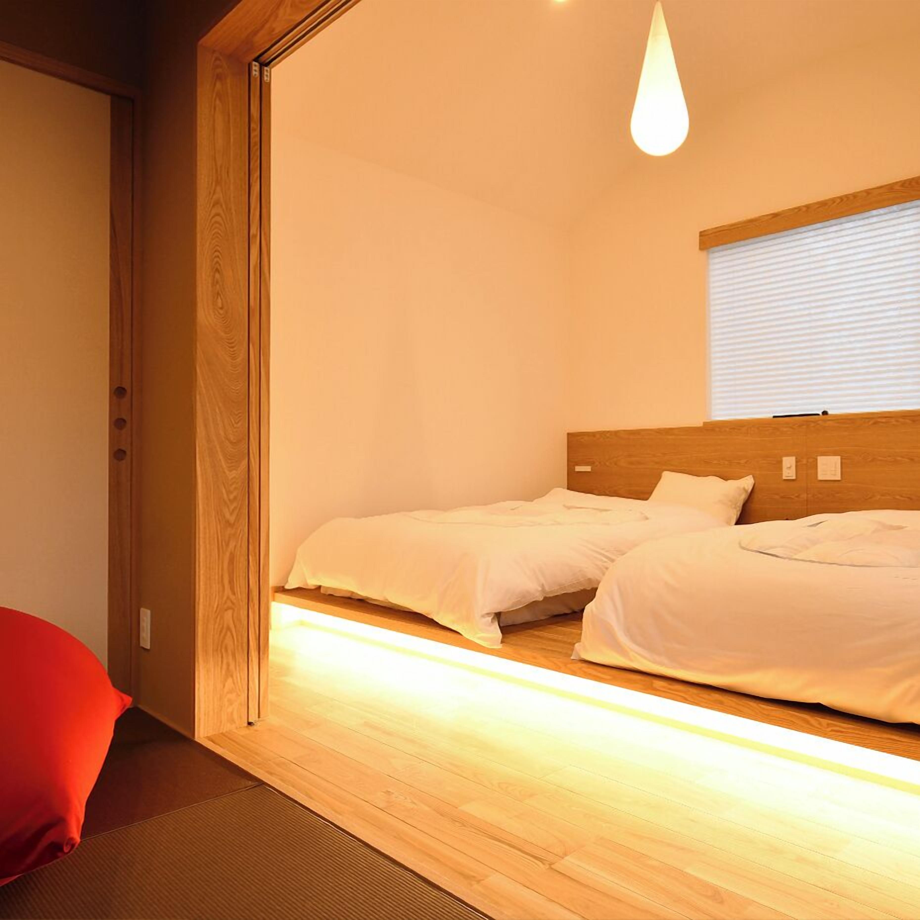 A bedroom with two beds, a wooden headboard, a window with blinds, and a hanging light fixture.