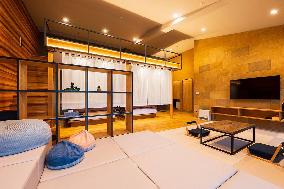 Un salon moderne comprenant un canapé, une table basse, un téléviseur fixé au mur et une cloison en bois avec une fenêtre.