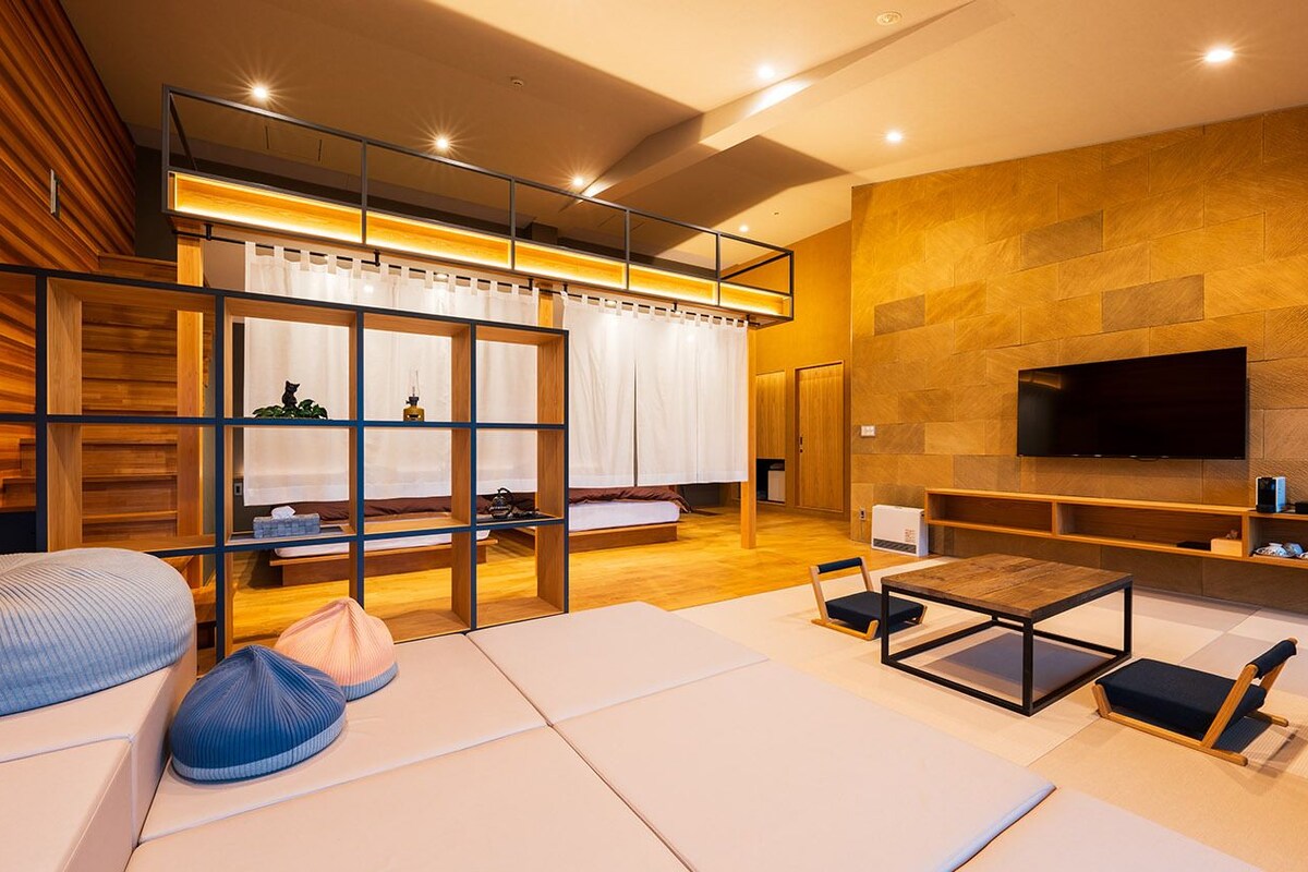 Una sala de estar moderna con un sofá, una mesa de centro, un televisor montado en la pared y un separador de madera con un ventanal.