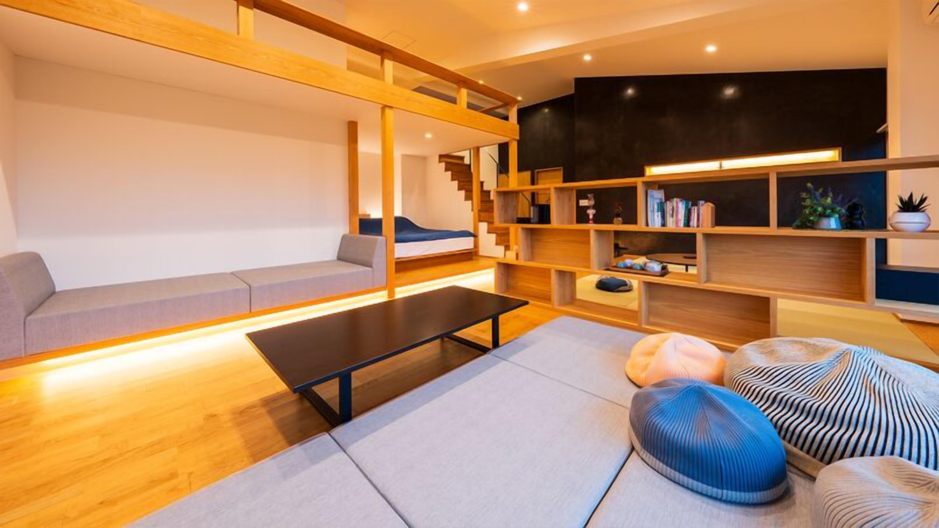 A modern living room with a sofa, a coffee table, a bookshelf, and a staircase.