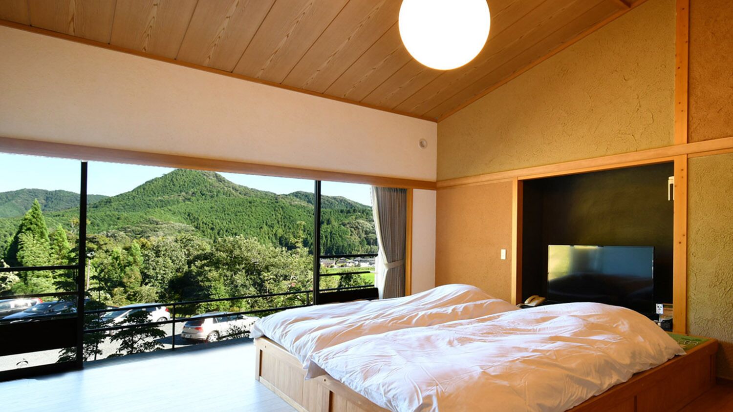 A bedroom with a large window, a bed, and a TV.