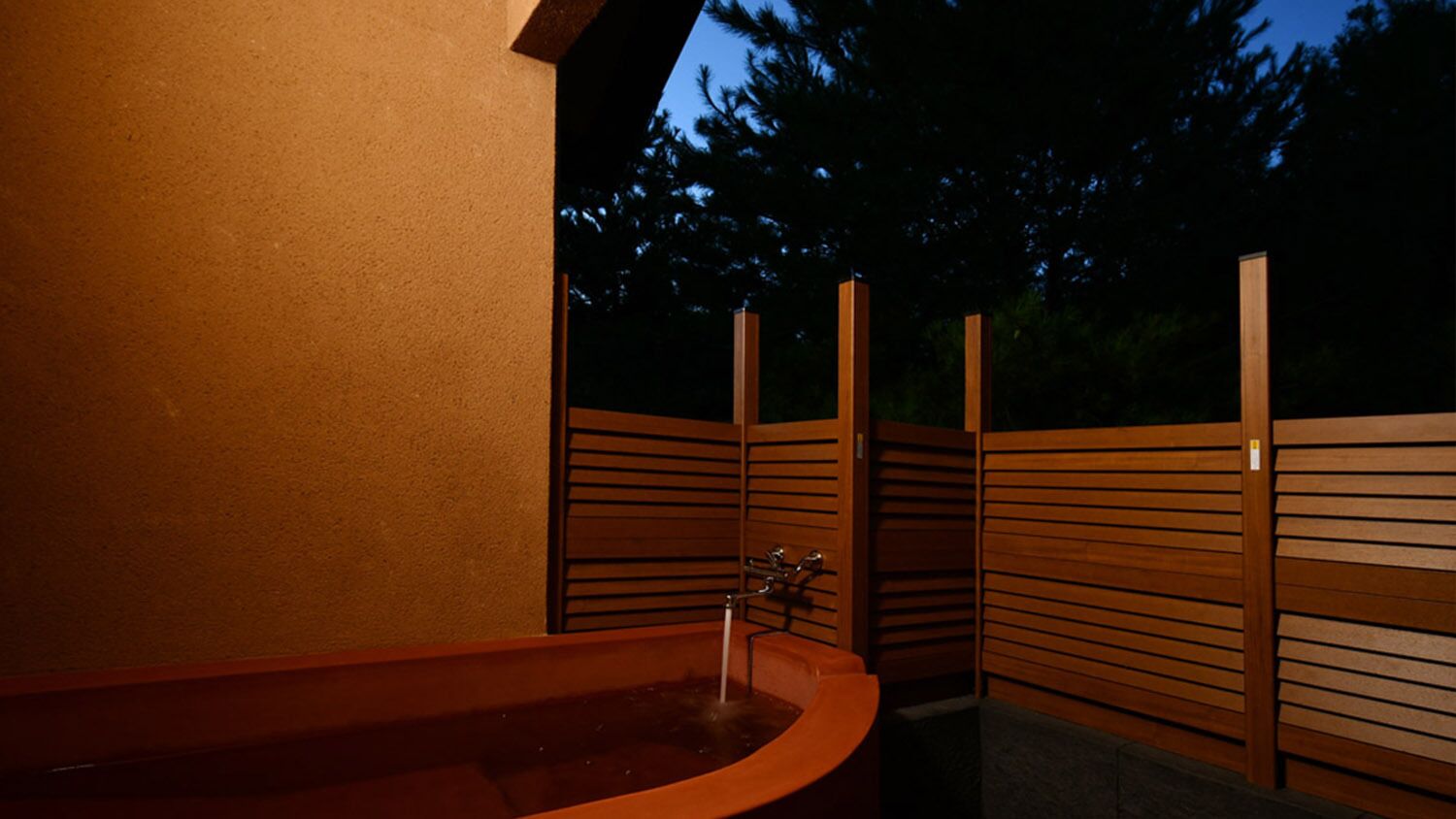 A spa area with a hot tub, wooden slatted walls, and a metal faucet.