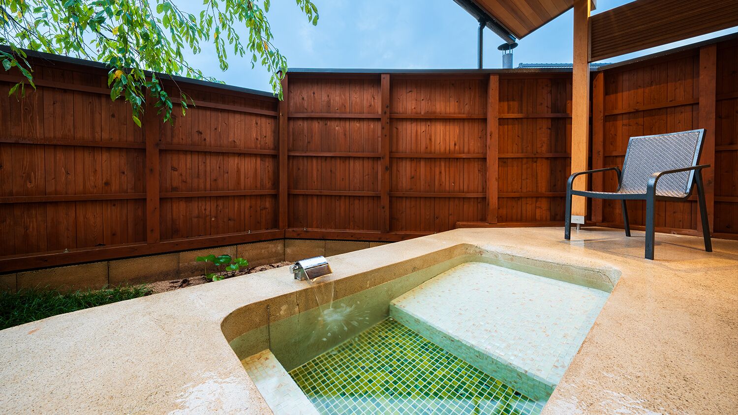 A backyard with a rectangular hot tub, a wooden fence, and a metal chair.