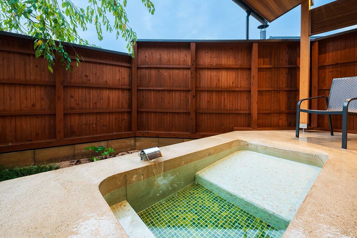 Un jardin avec un jacuzzi rectangulaire, une clôture en bois et une chaise en métal.