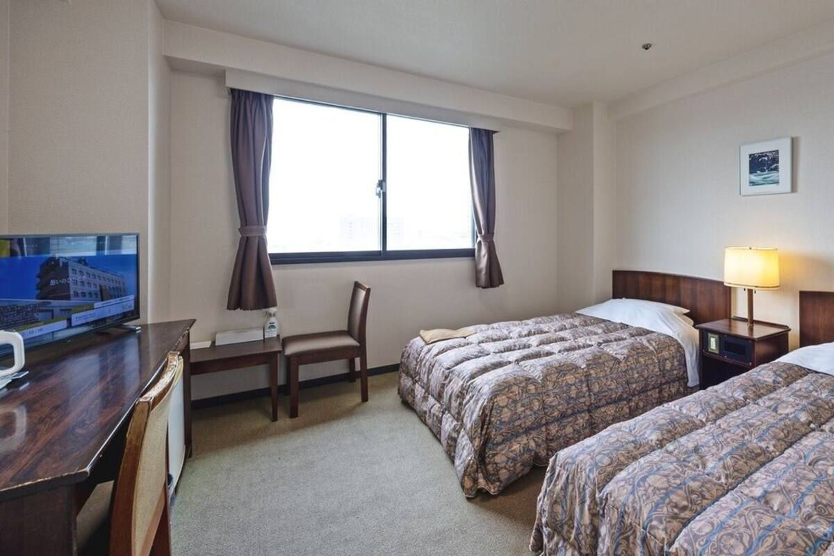 Habitación de hotel con dos camas, un escritorio, una silla, un televisor y una ventana con cortinas.