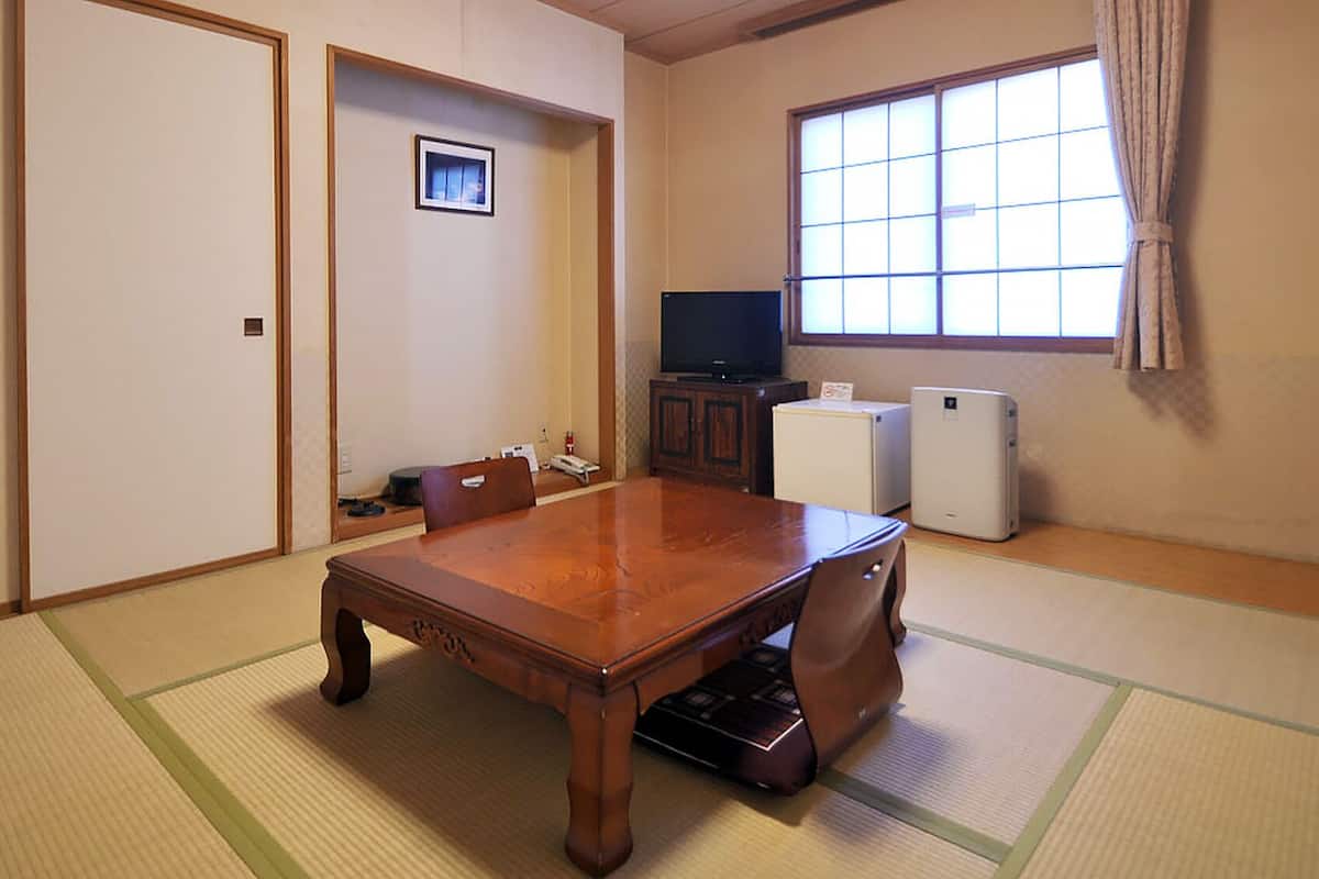 Perinteinen japanilaistyylinen huone, jossa on tatamimatto, puinen ruokapöytä, televisio ja pieni jääkaappi.