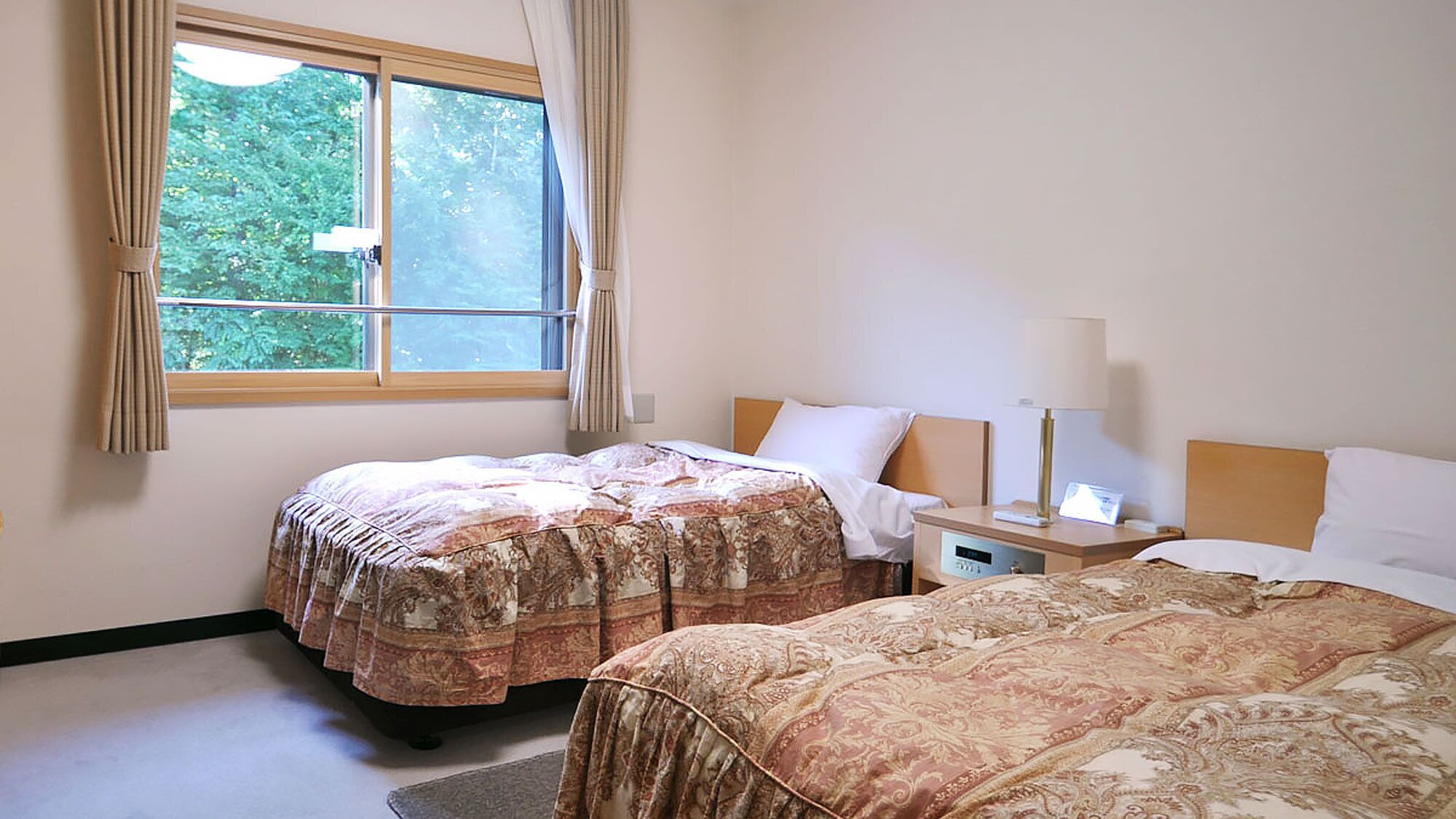 Een hotelkamer met twee bedden, een raam met gordijnen, een nachtkastje met een lamp en een wandklok.