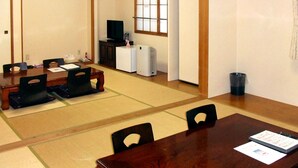 Una habitación de estilo japonés tradicional con suelo de tatami, una mesa baja con sillas, un televisor y un refrigerador pequeño.