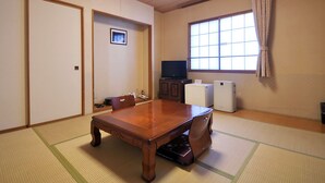 Una habitación tradicional japonesa con suelo de tatami, una mesa de madera para comer, un televisor y un refrigerador pequeño.