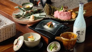A traditional Japanese meal setup with various dishes, a bottle, and a teapot on a wooden table. - Kyoya (Takayama)