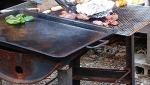 A grill with food being cooked, a bottle of sauce, and a container of spices on a table. - Ichinokuraso Bettei Shirouma (Hakuba)