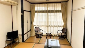 A small room with tatami mats, two chairs, a table, a TV, and a window with curtains. - Eco Hotel Yunokoso (Minamata)