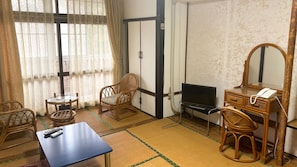 A traditional Japanese-style room with tatami flooring, a television, a desk with a telephone, and two chairs. - Eco Hotel Yunokoso (Minamata)
