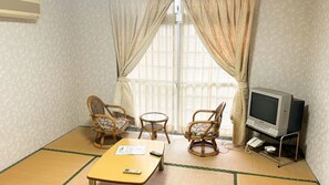 Ein Zimmer mit Fernseher, zwei Korbstühlen, einem kleinen Tisch und einem Boden aus Tatami-Matten.
