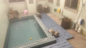 Ein kleiner, rechteckiger Pool mit Fliesenboden und einigen Gegenständen in der Nähe, darunter ein pinkfarbener Hocker und Flaschen auf einem Regal.