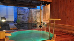 A hot tub with a stone wall backdrop and wooden flooring. - Seishohtei Shirasuna (Shirako)