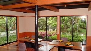 A modern dining area with wooden tables and chairs, large windows offering a view of greenery and trees. - Seishohtei Shirasuna (Shirako)