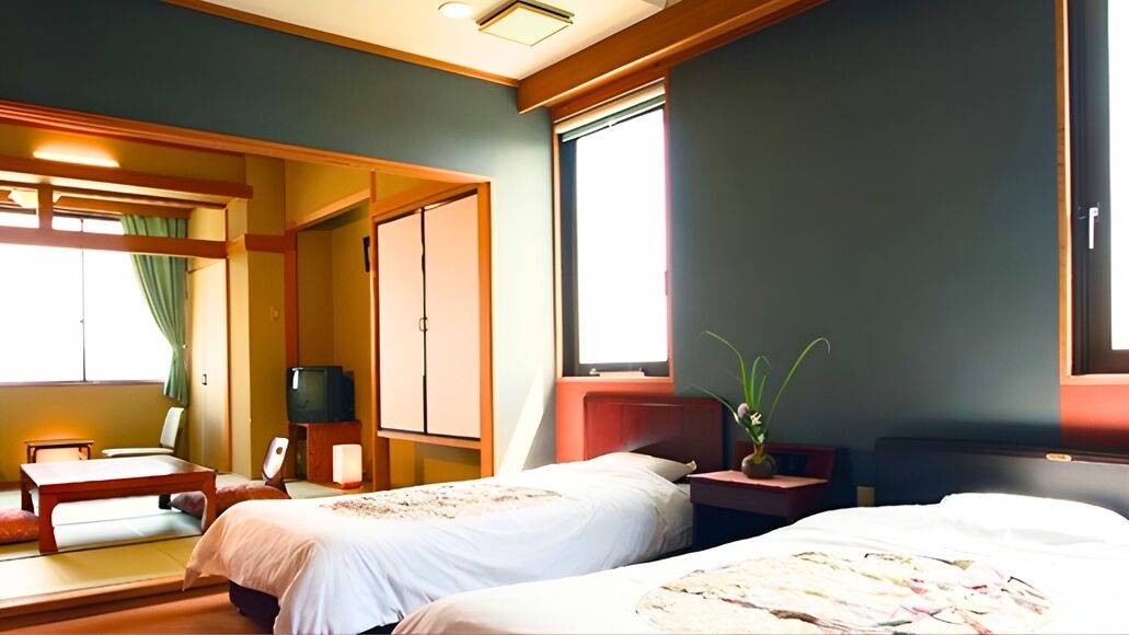 Quarto de hotel com duas camas, televisão, escrivaninha e janela.