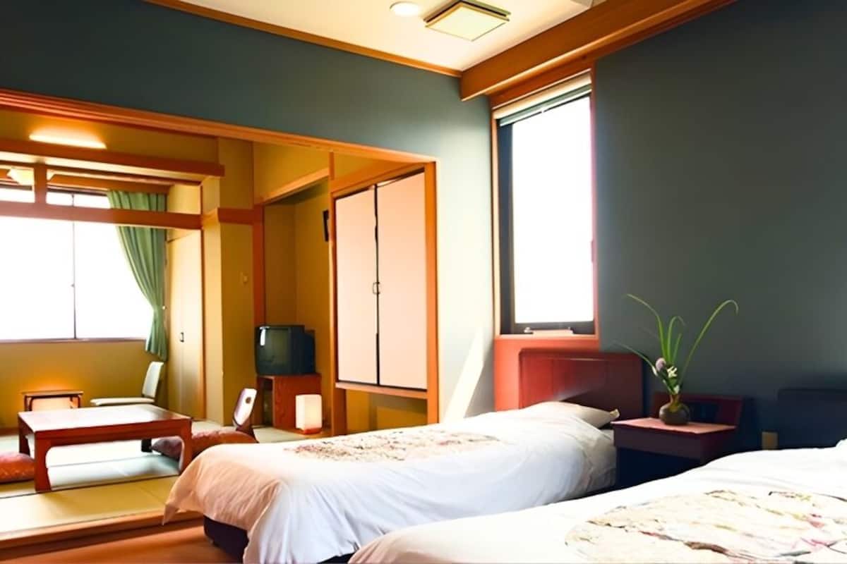 A hotel room with two beds, a TV, a desk, and a window.