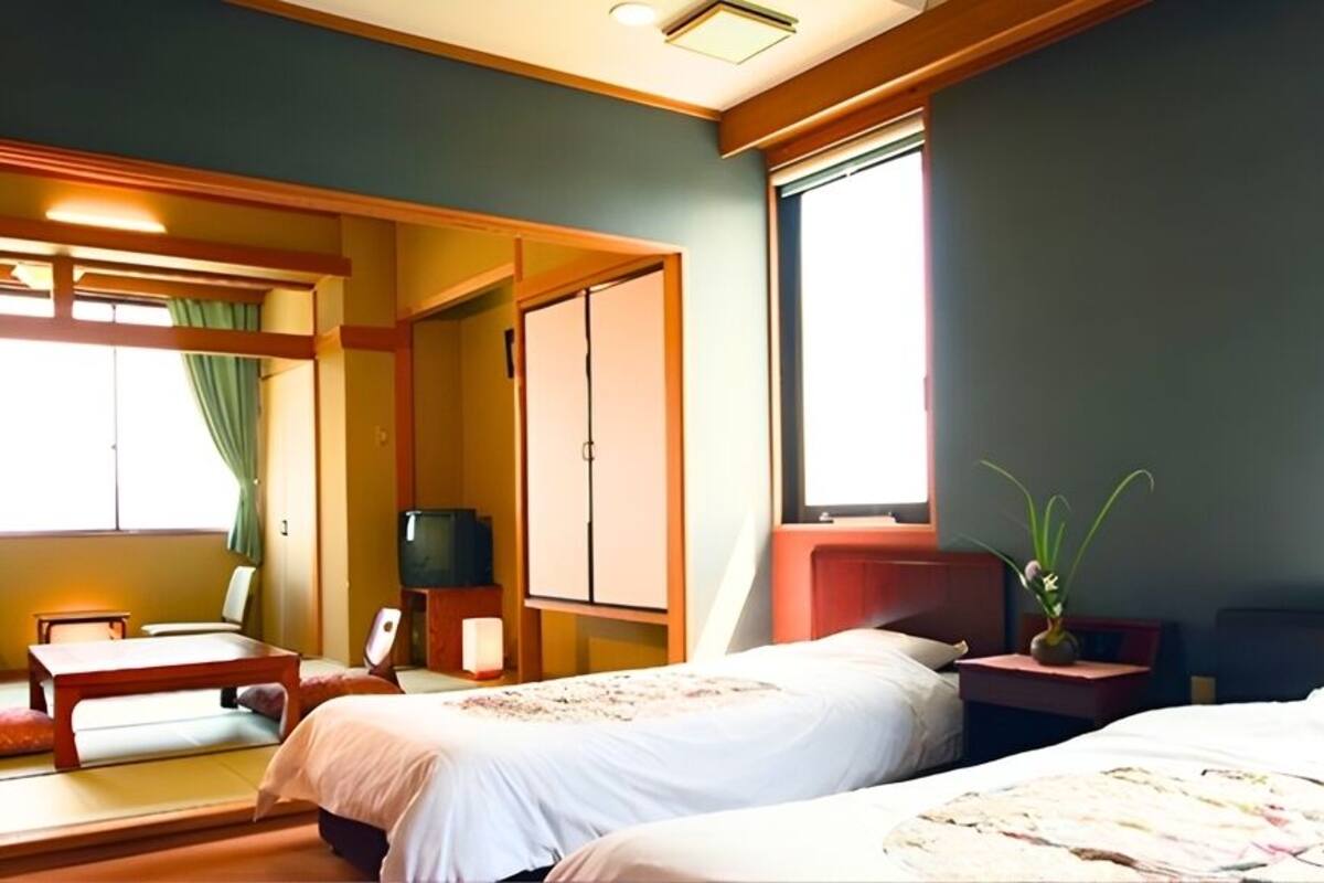 Quarto de hotel com duas camas, televisão, escrivaninha e janela.