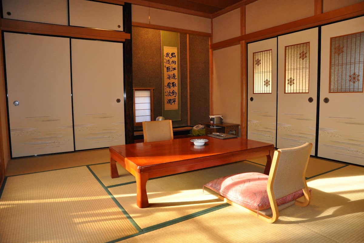 A traditional Japanese room with tatami flooring, a wooden table, a chair, and sliding doors with decorative glass panels.