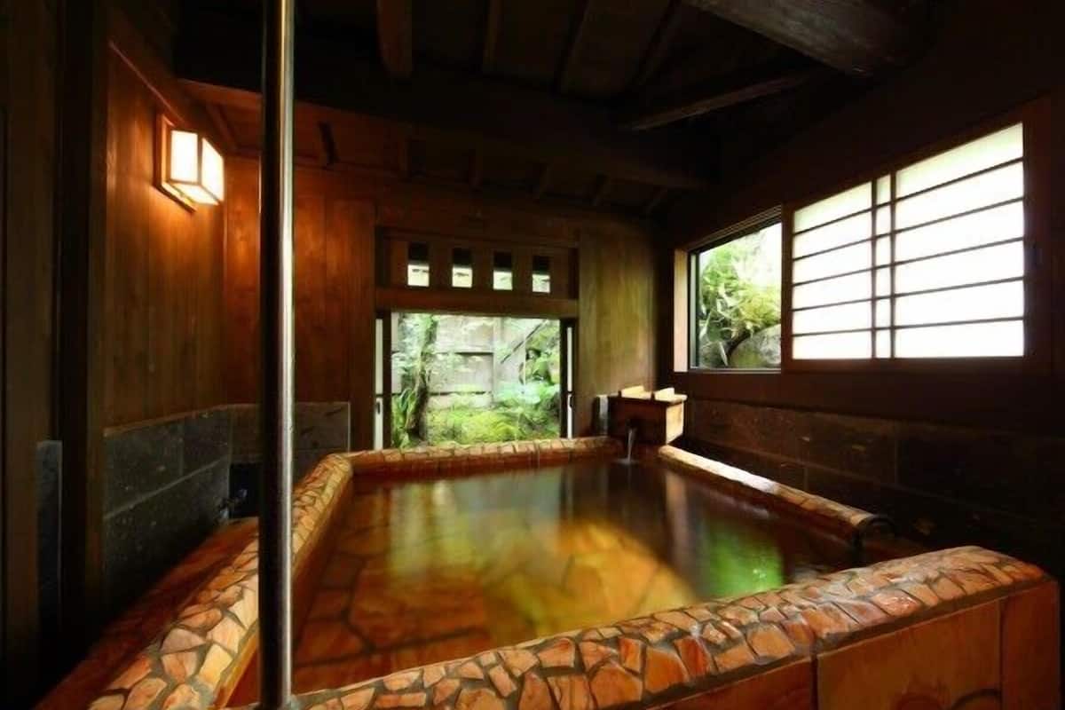 Un onsen japonés tradicional con un baño de piedra, paredes de madera y vistas a la vegetación.