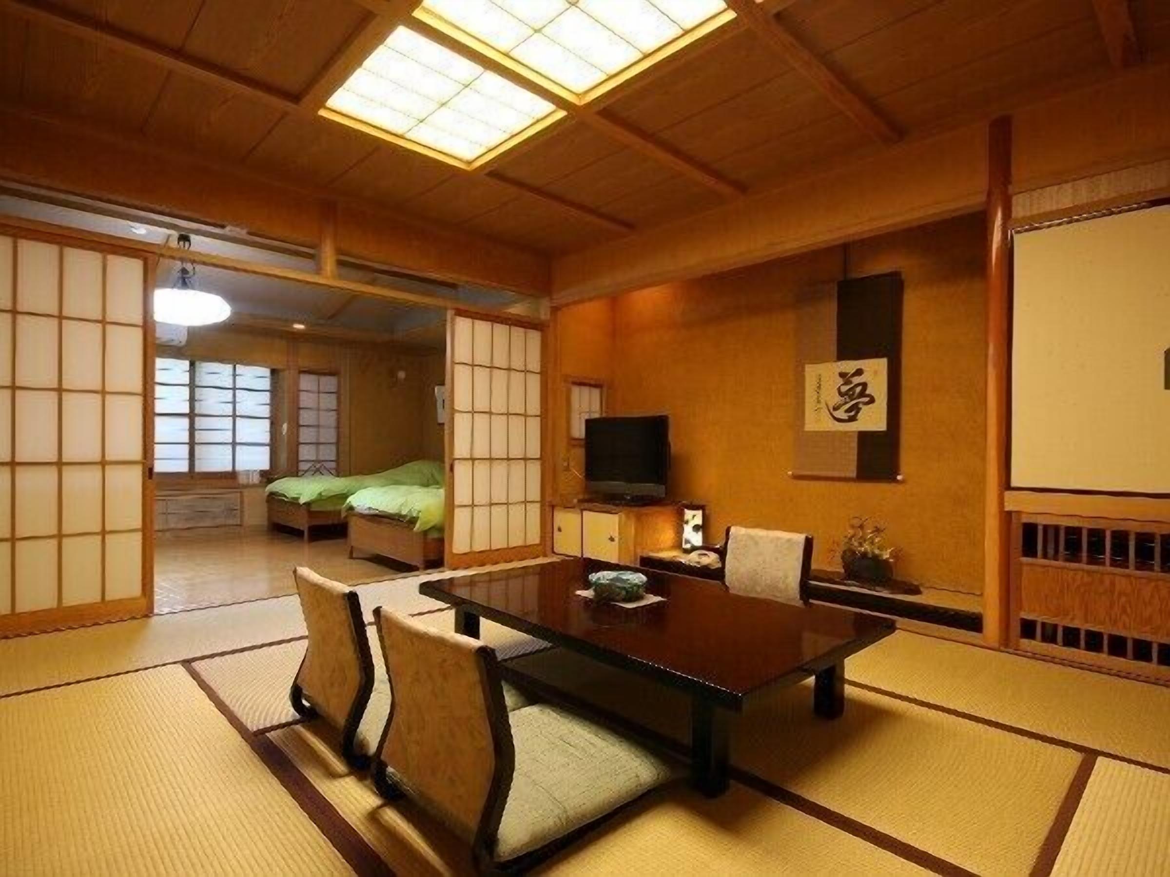 A traditional Japanese room with tatami flooring, a low table with chairs, a television, and sliding doors.
