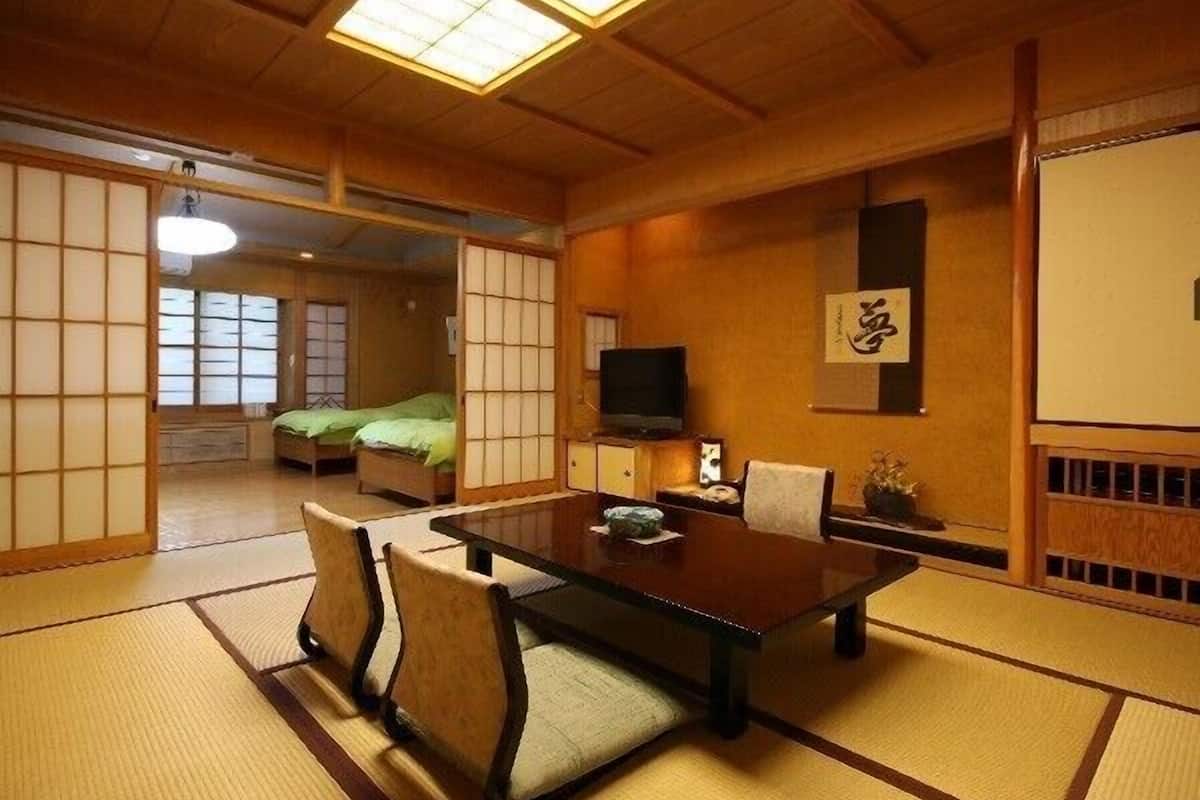 Una habitación japonesa tradicional con suelo de tatami, una mesa baja con sillas, un televisor y puertas correderas.