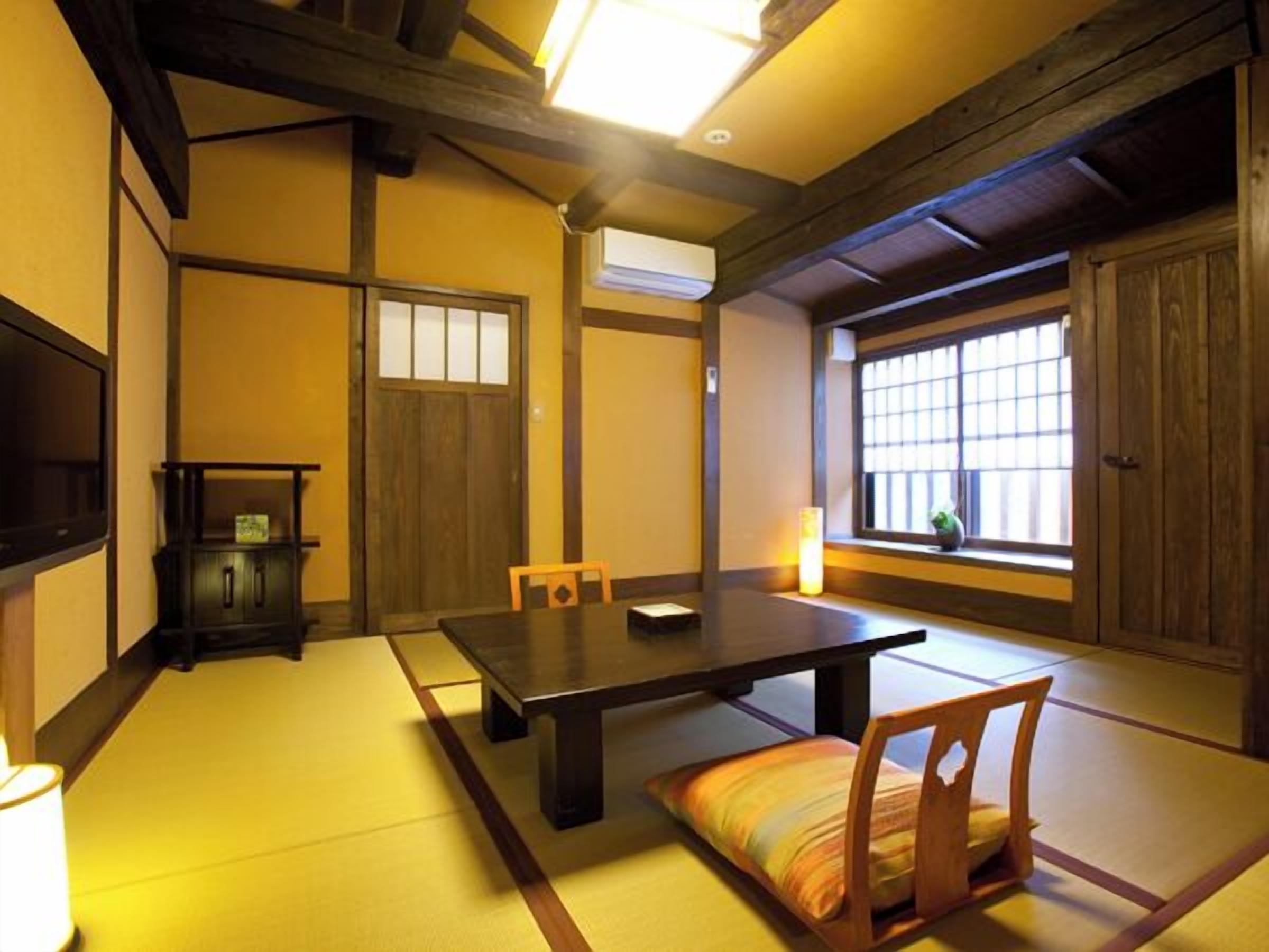 A traditional tatami mat room with a low table, chairs, a clock, and a window with a view.
