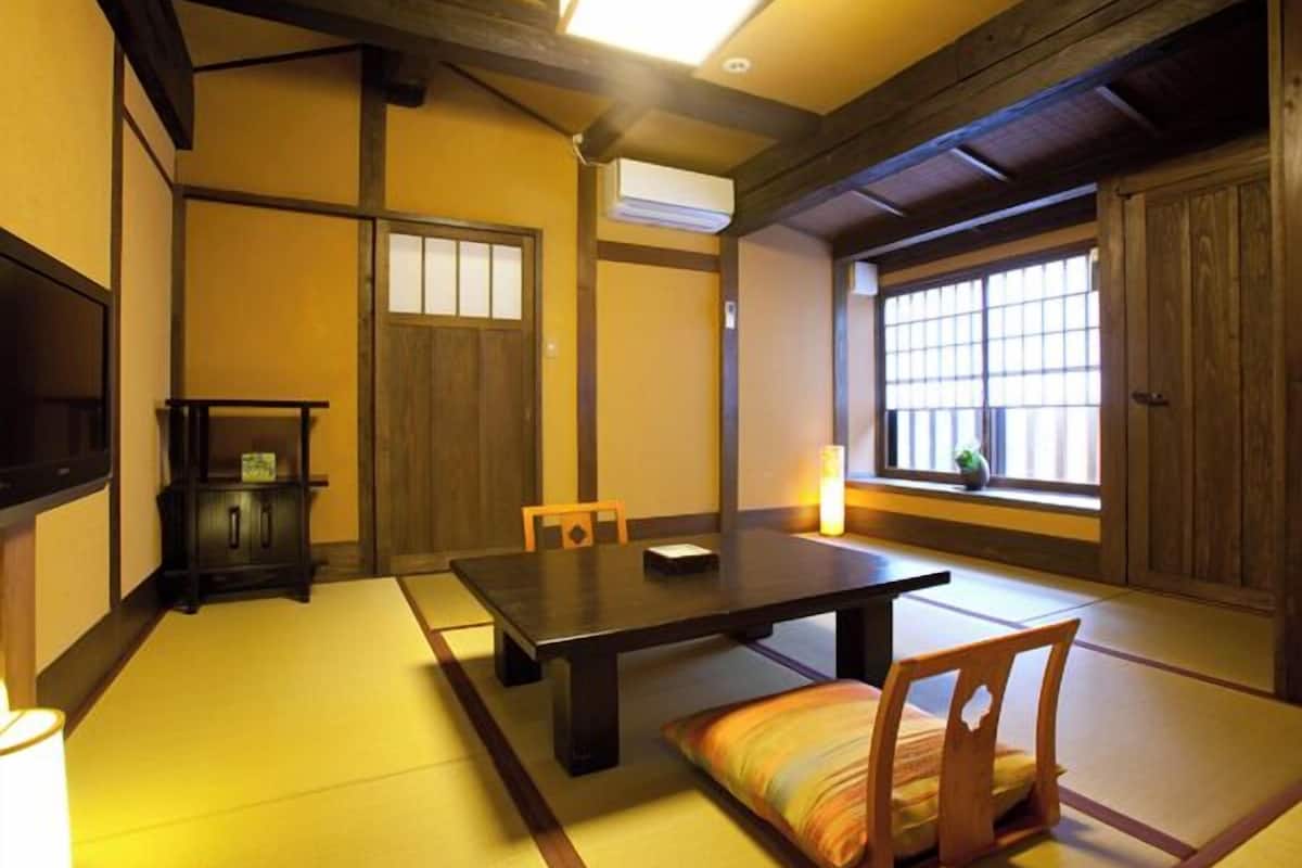 Un espacio tradicional con esteras de tatami, una mesa baja, sillas, un reloj y un ventanal con vistas.