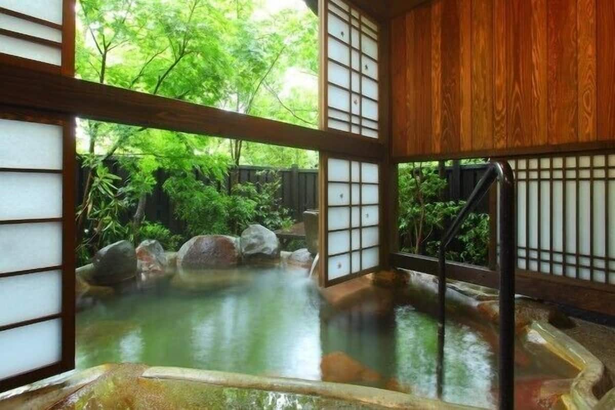 Un onsen japonés tradicional con puertas correderas de madera y vistas a un follaje exuberante.