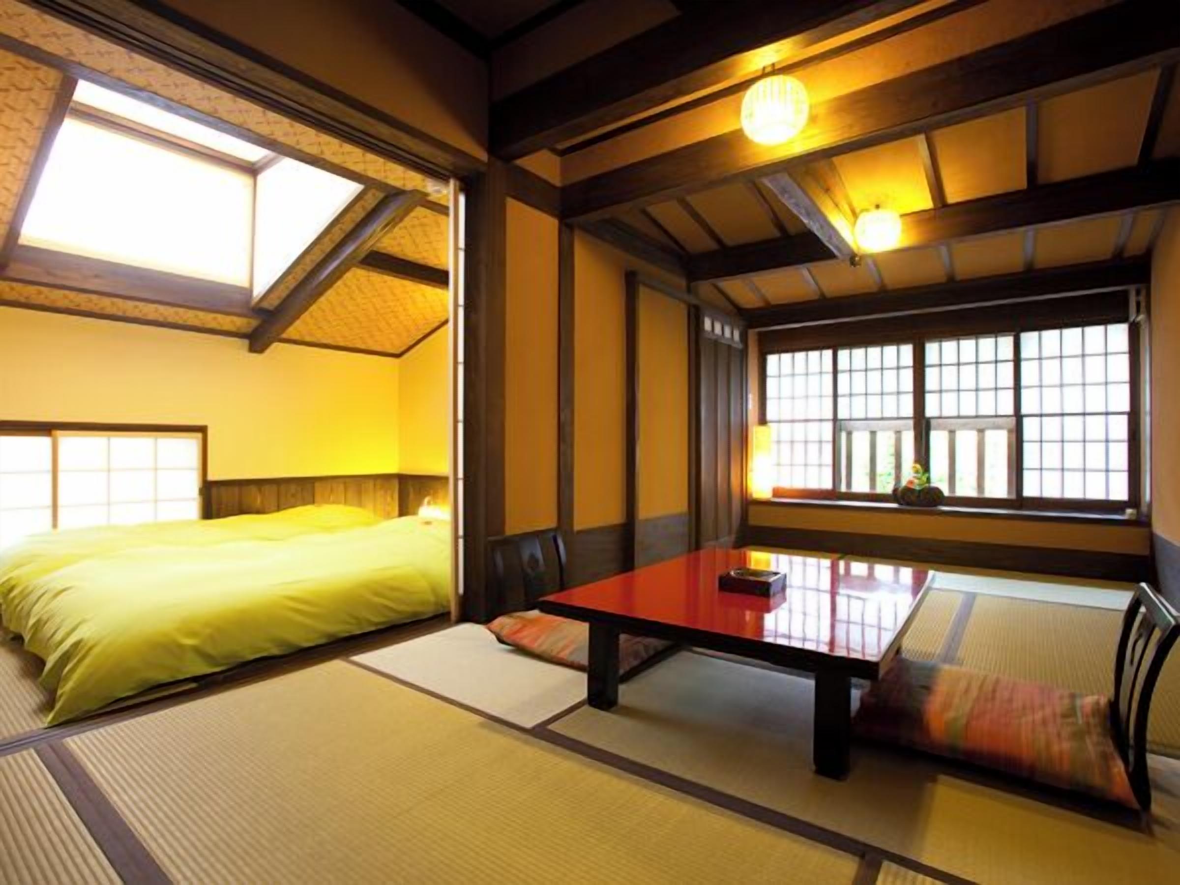 A traditional Japanese room with tatami flooring, a low table, and a bed with a yellow bedspread.