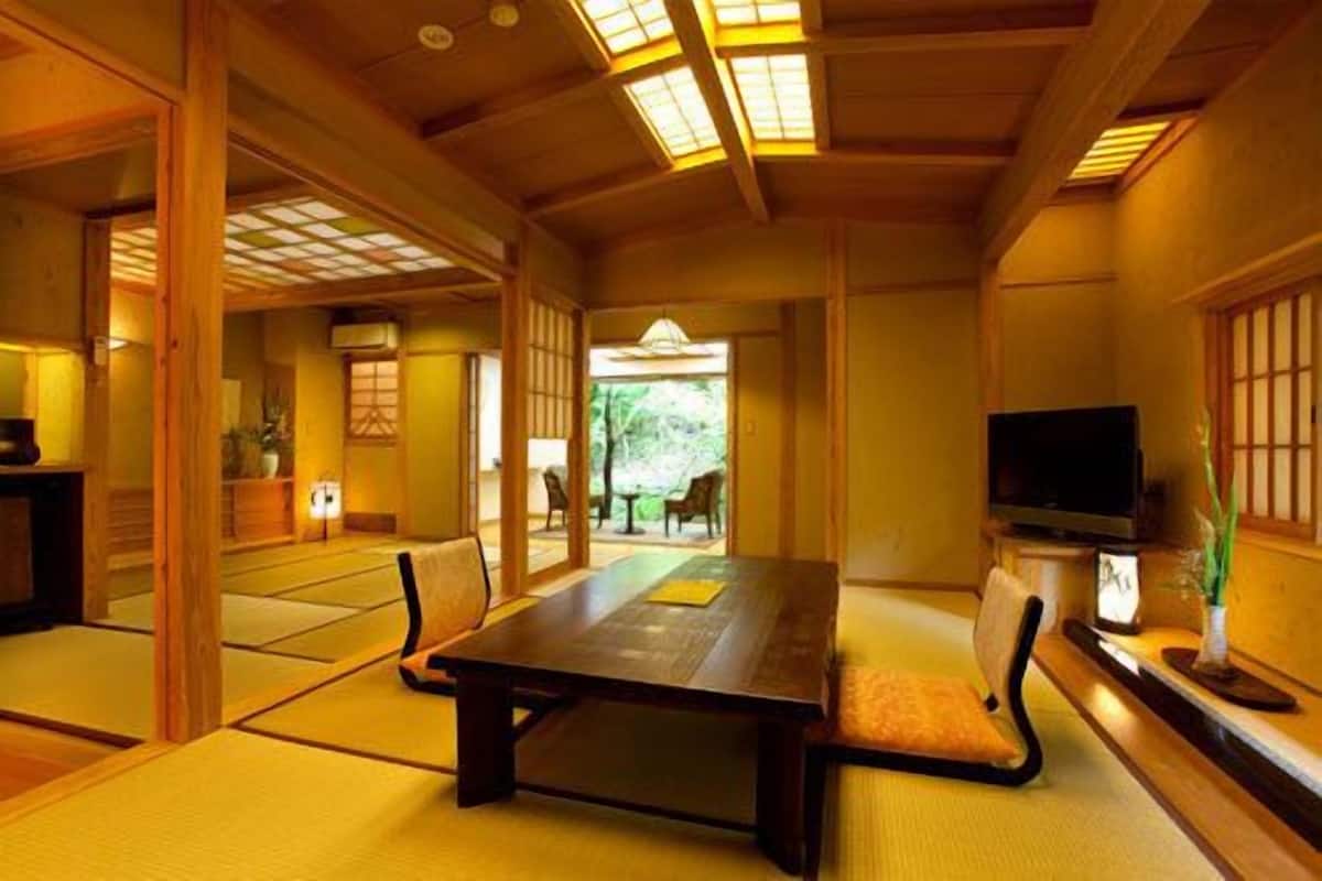 Una habitación japonesa tradicional con suelo de tatami, una mesa baja, un televisor y vistas a un jardín.