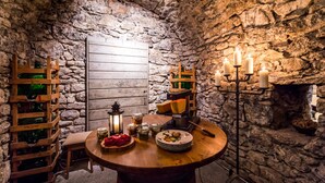 Une pièce rustique aux murs de pierre, avec une table en bois dressée pour le repas, des appliques murales pour bougies et une lanterne.