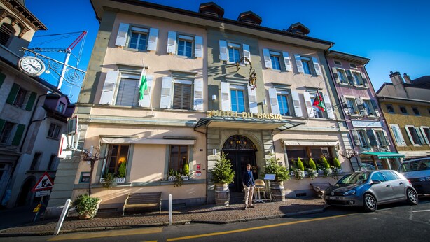 Un hôtel à la façade classique, orné d’une horloge et d’une enseigne indiquant « HÔTEL DU RAISEIN ».