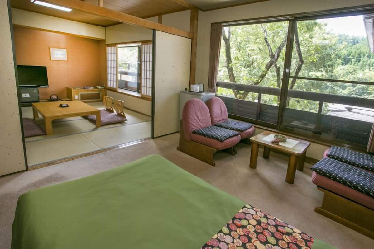 A room with a bed, a wooden table, two chairs, a small table with a cup, and a window with a view of trees.