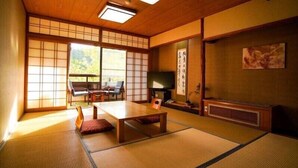 A traditional Japanese room with tatami flooring, a low table, chairs, a television, and sliding doors. - Kurokawa Onsen Wafu Ryokan Misato (Minamioguni)