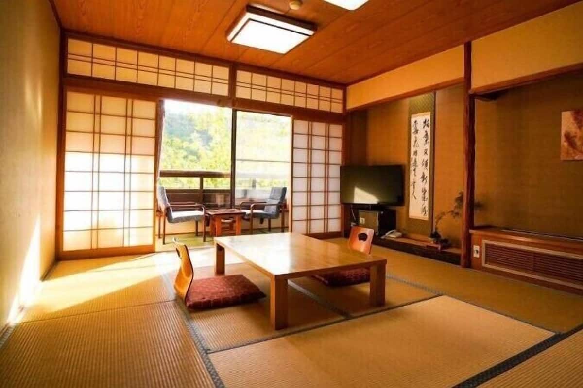 A traditional Japanese room with tatami flooring, a low table, chairs, a television, and sliding doors.
