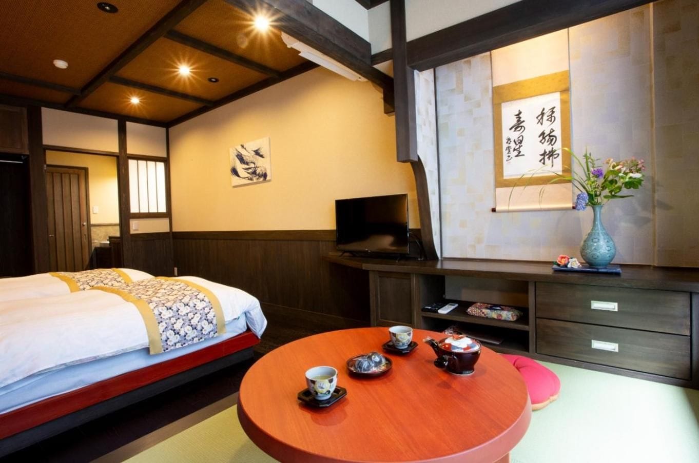 A traditional Japanese room with two beds, a wooden table with tea set, and a television.