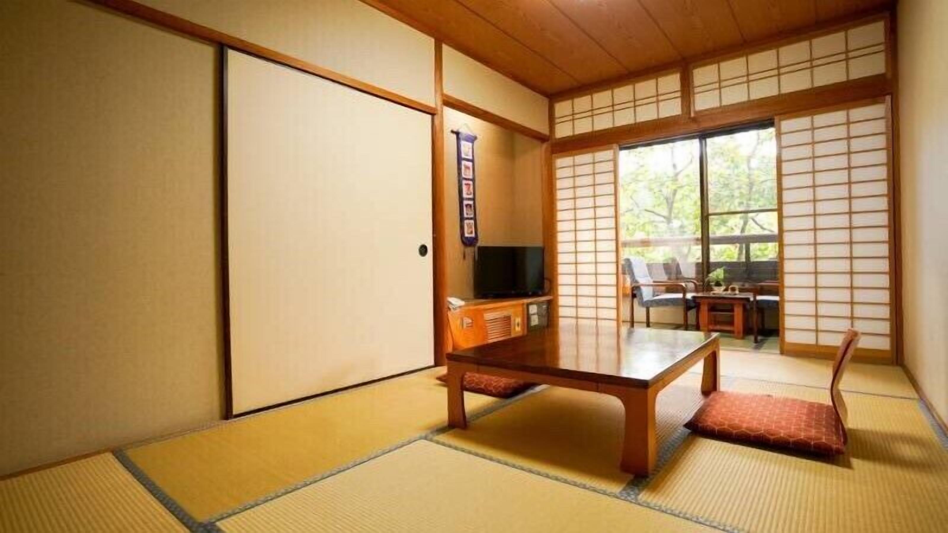 Una habitación japonesa tradicional con suelo de tatami, una mesa de madera baja, un televisor y puertas correderas.