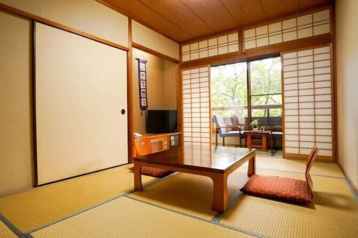A traditional Japanese room with tatami flooring, a low wooden table, a television, and sliding doors.