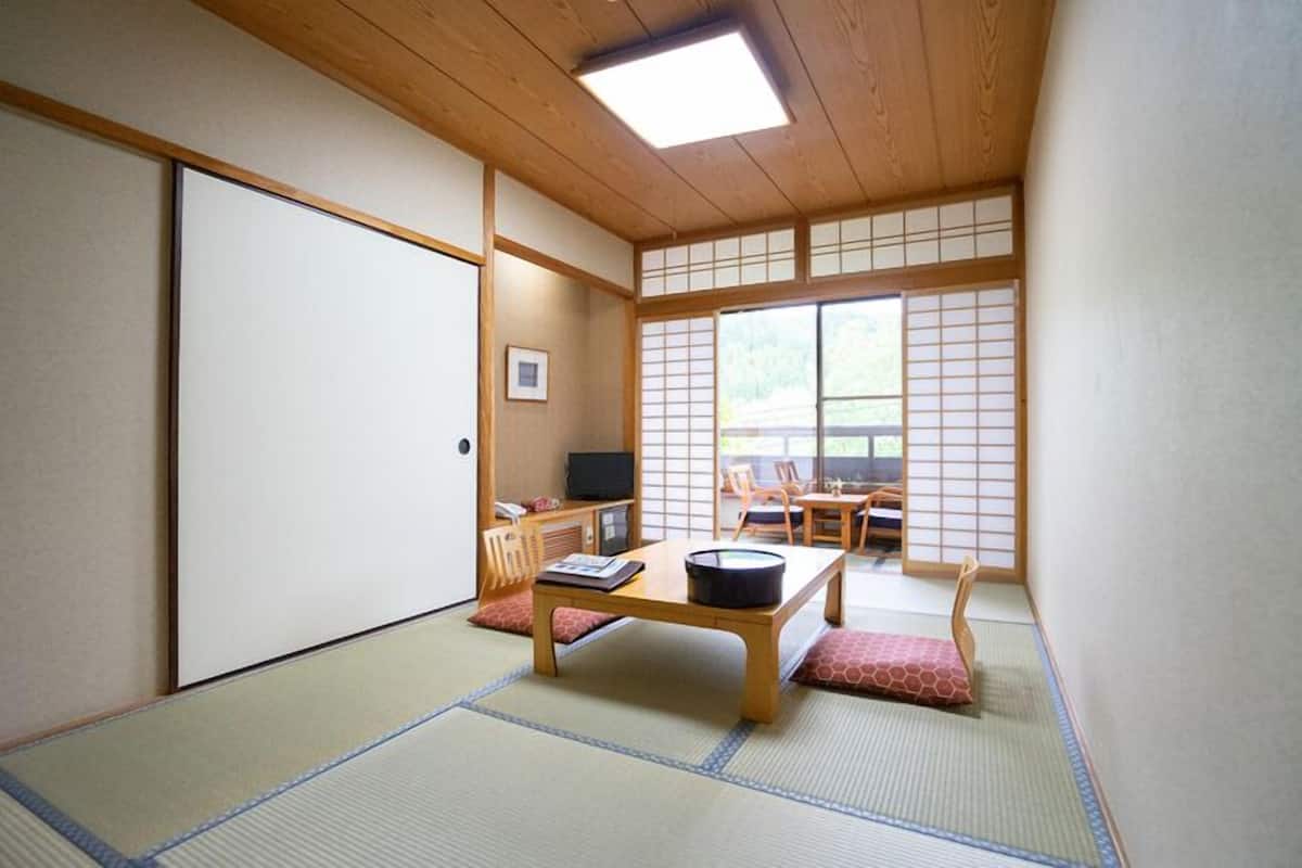 A traditional Japanese room with tatami flooring, a low table with a black pot, a television, and a sliding door.