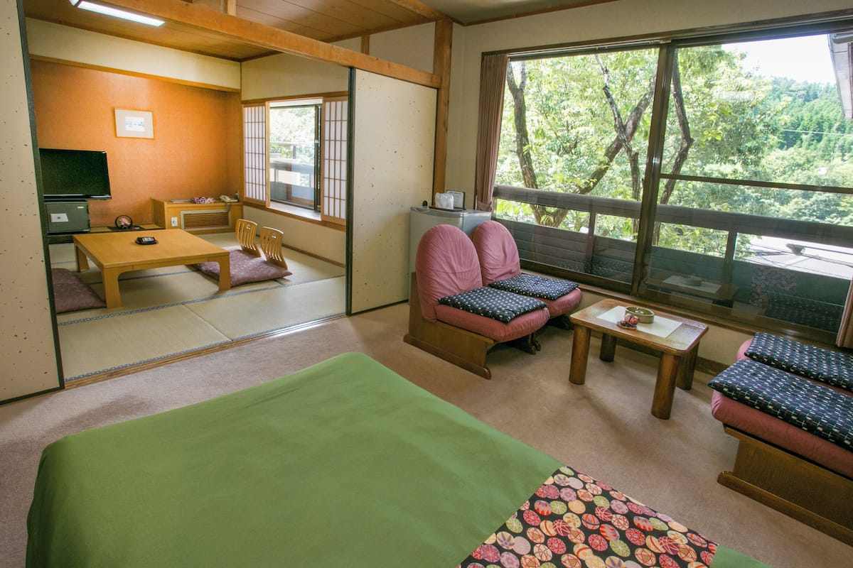 A traditional Japanese-style room with tatami flooring, a low table, a sofa with cushions, and a view of greenery outside.