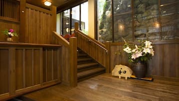 A wooden staircase with a handrail leading to a landing area with a small table and a vase of flowers.